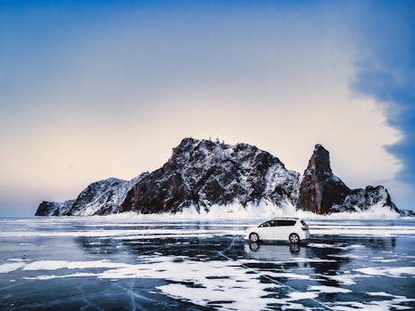 A car parked on the frozen surface of Lake Baikal against a rocky island, capturing winter's icy beauty.